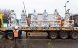 A lorry transporting six large stone statues. A person in PPE and high-vis vest is standing nearby watching the statues arrive.