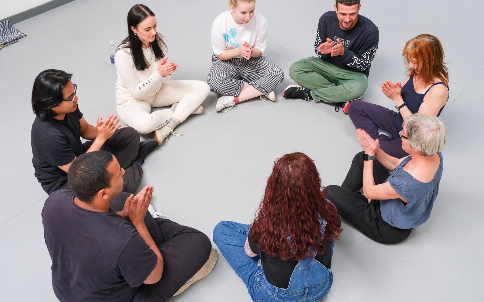 A group of people sit in circle with their hands together, as if in prayer.