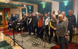 A group of people standing in a recording studio. They are smiling at the camera.