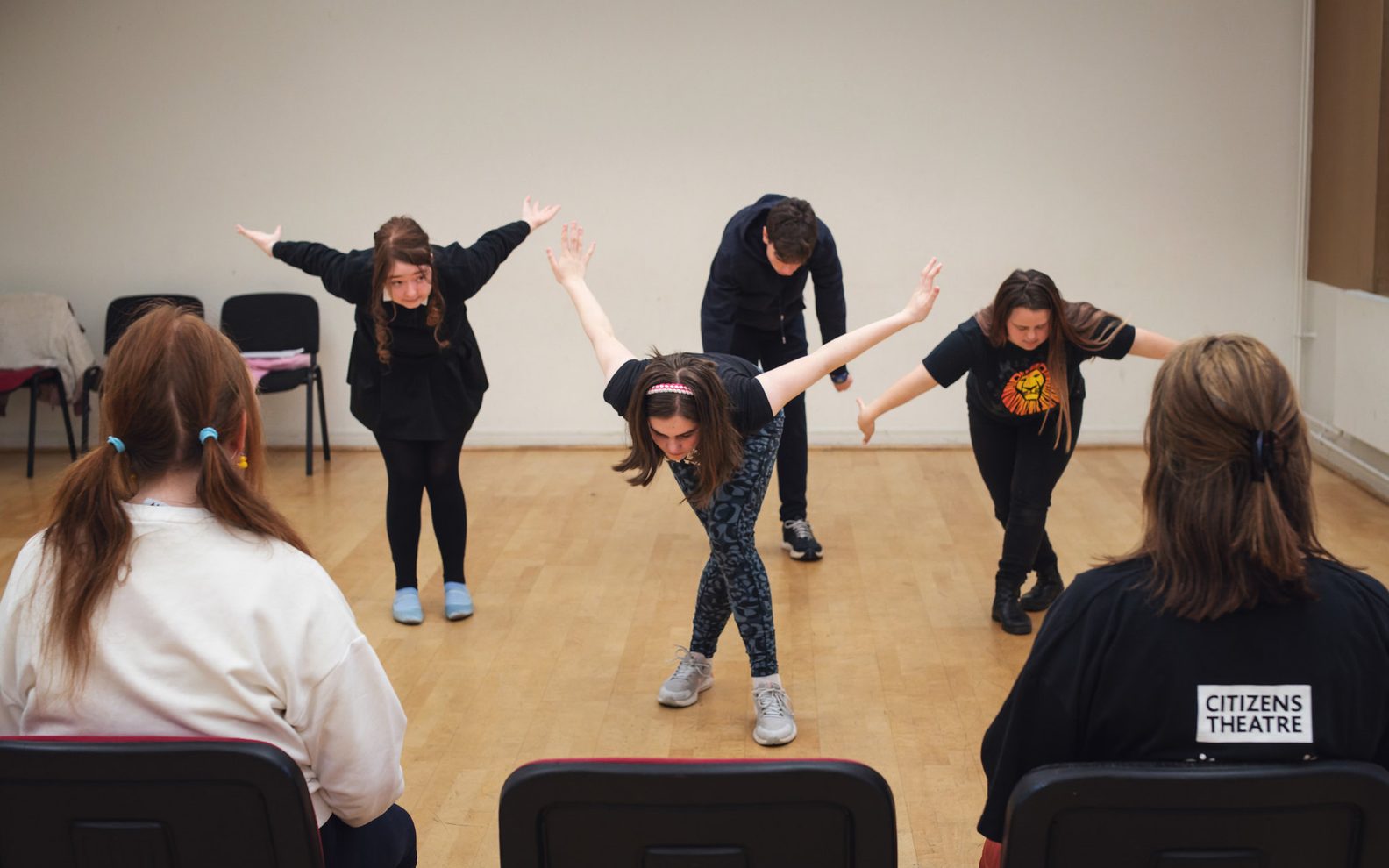Four people bowing. In the foreground audience members are sitting watching the performance.