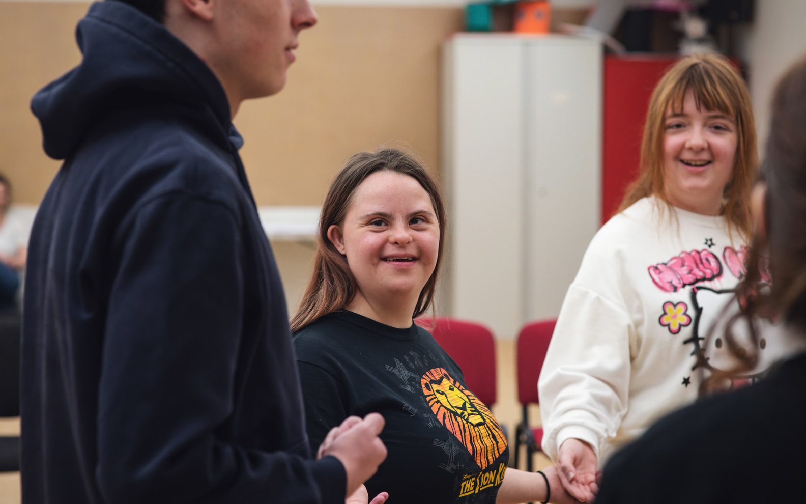 Three learning disabled young people taking part in a drama game. They are holding their hands out and are smiling.