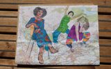 A colourful felt-tip drawing of three women, one sitting on a chair and two posing dramatically, drawn onto a map.