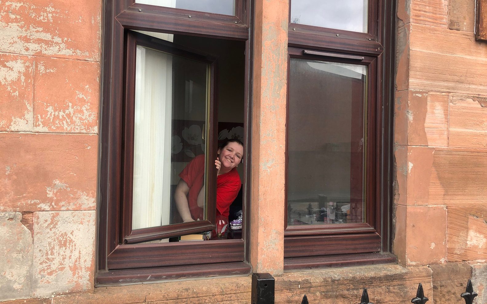 A woman smiles from her window in a Glasgow red brick tenement.