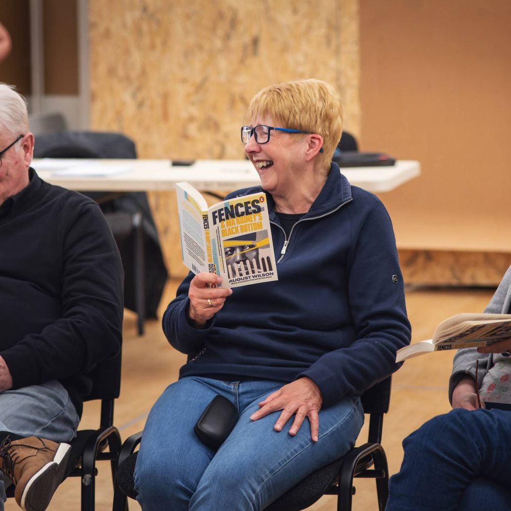 A play reading session. Two women and a man sitting in a row and holding copies of the play 