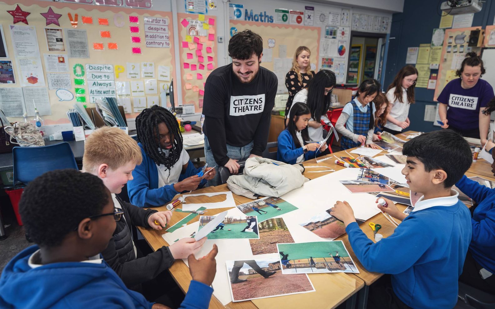 A busy classroom. Primary pupils are sitting around a table cutting out pieces of paper and chatting.