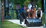 Performers in a large-scale outdoor event. They are wearing old fashioned clothing and rolling a barrel.