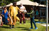 An outdoor event. A First Nation storyteller is handing a football to a young boy.