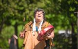 A First Nation storyteller standing outside playing a percussion instrument.