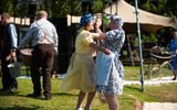 An outdoor performance. Two women in costume are dancing arm in arm.