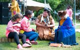 Performers at an outdoor event. First Nation storytellers from Manitoulin Island are sitting on the ground with two young people.