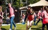 A group of young performers at an outdoor event. They are running and smiling. One person is being carried on another's back.