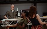 Actors rehearsing for Sweat. Two women are dancing back to back and a man is standing watching them from behind a bar.