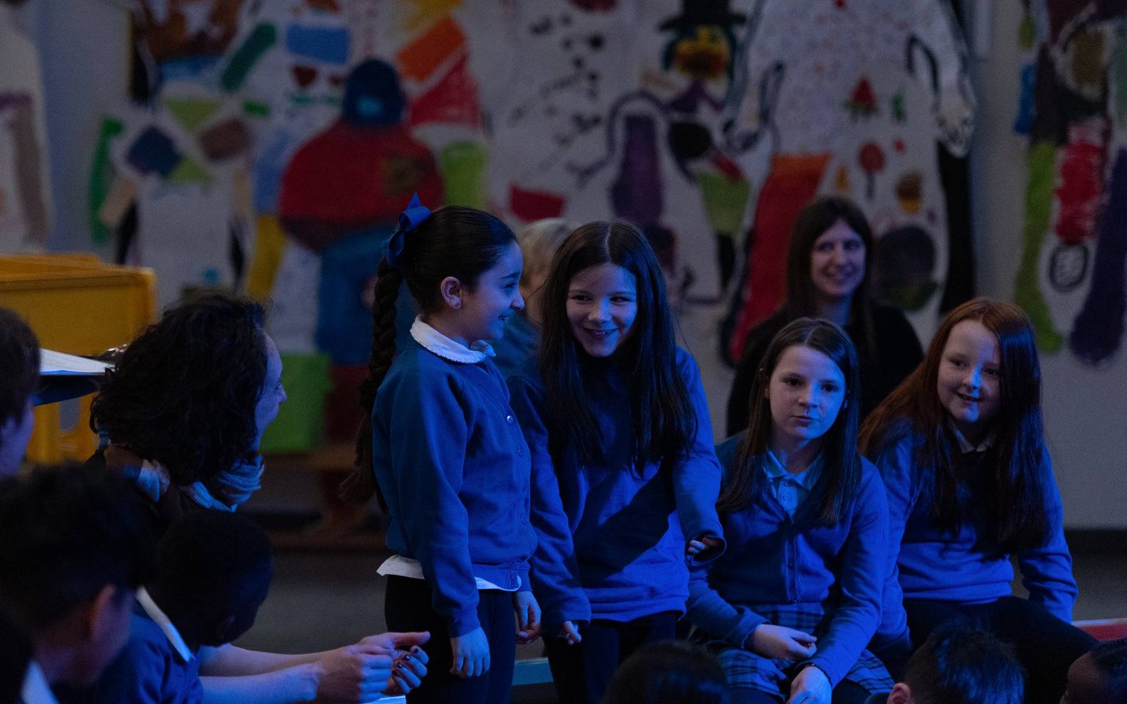 A group of school pupils in blue jumpers are standing together smiling and laughing