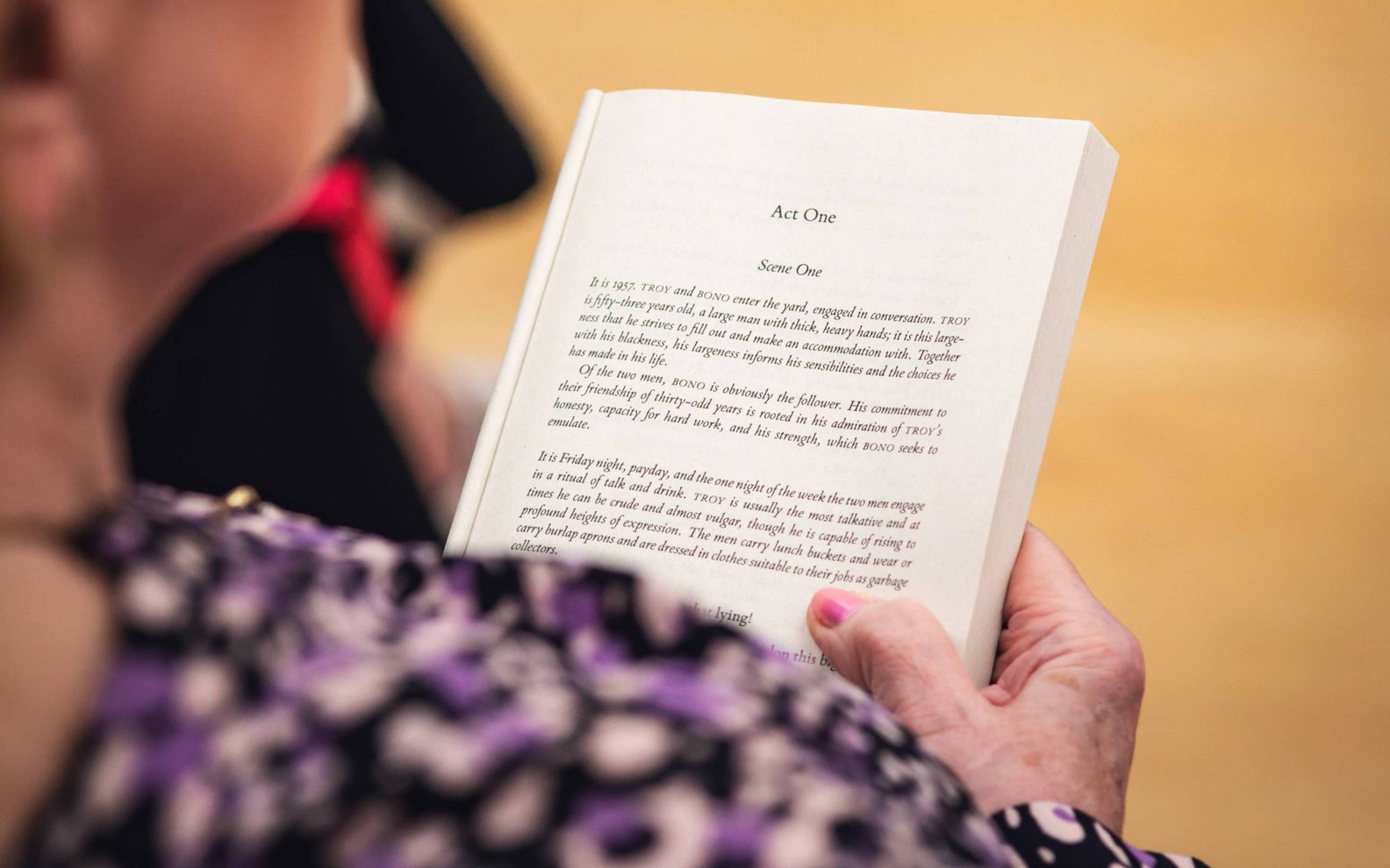 A play reading session. A woman holds a book open, with the first page in focus.
