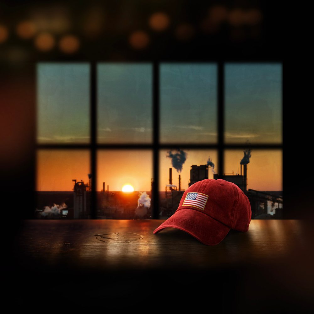 An American cap sitting on a table. Behind is a window where you can see a sunset and indistrial chimney.
