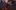 28132743537_402fa87023_c-aspect-ratio-1600-1000 A young toddler is walking towards the camera. She is holding a bunch of red and yellow balloons. Three adults are in the background smiling at her.