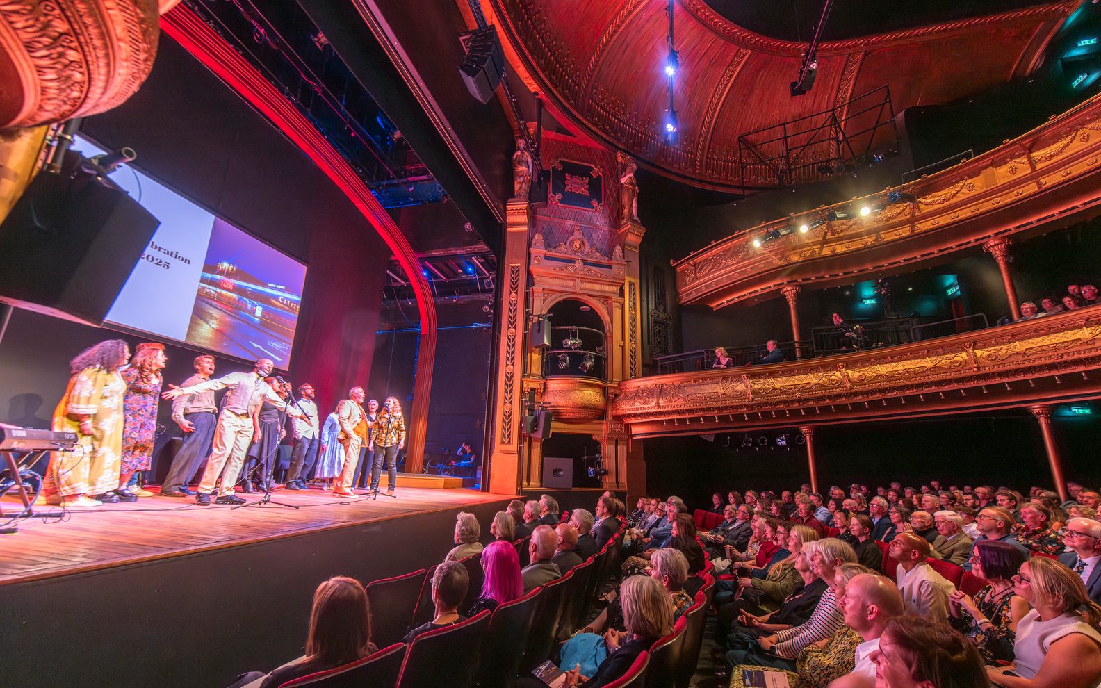 An auditorium with an audience watching perfomers on a stage