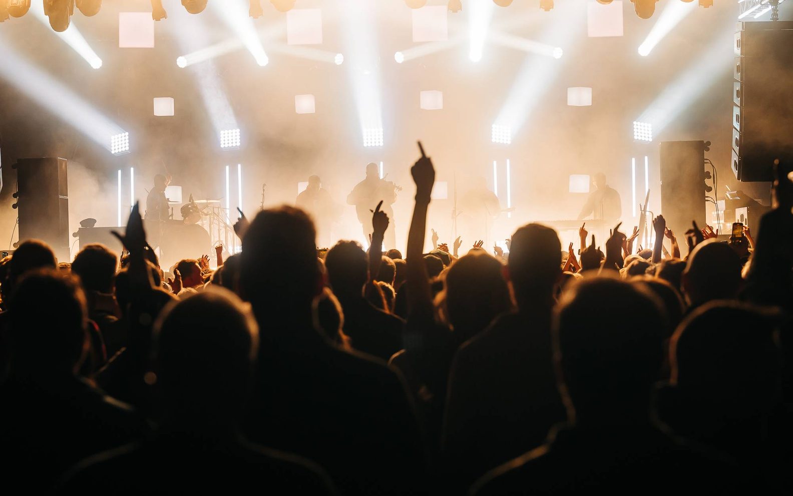 A crowed witharms in the air looking up at a bright stage