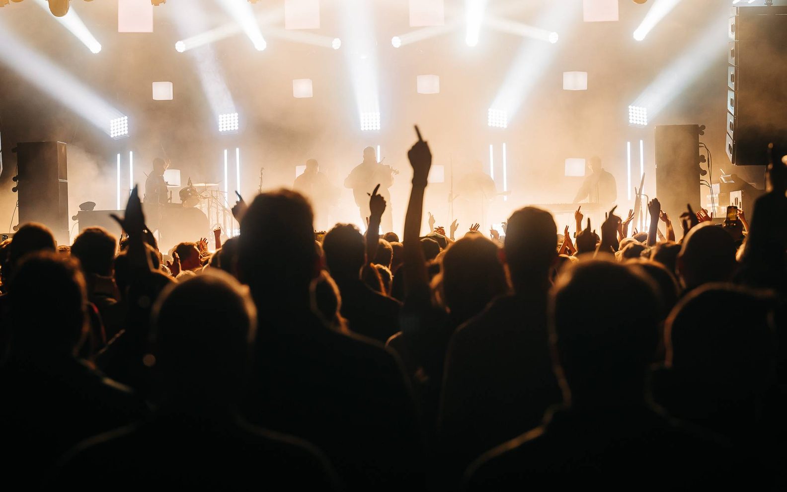 Celtic-Connections-generic-aspect-ratio-1600-1000 A crowed witharms in the air looking up at a bright stage