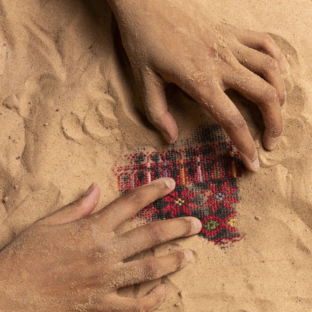 Hands digging in sand, uncovering a piece of decorative red fabric.