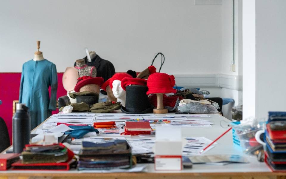 A selection of bits of costume on a table with lots of drawings of costumes