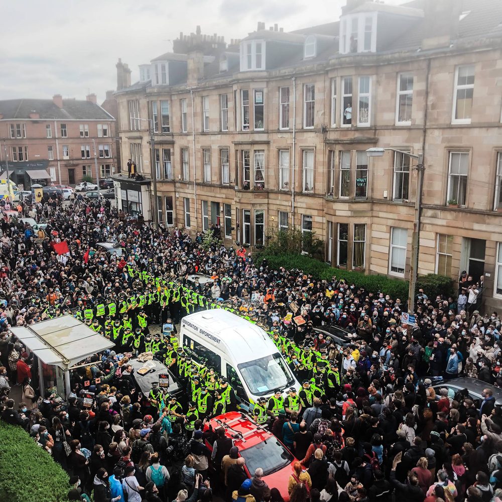 A group of people on a street in Glasgow, protesting around an Immigration Enforcement van.