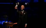 A performer stands on stage. He is throwing a pack of cards into the air.