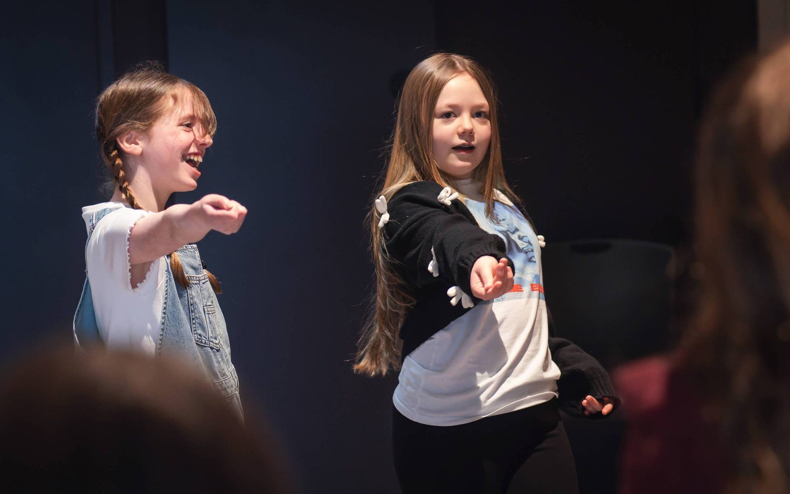 Two girls performing. They are both pointing to an audience with their right hand.